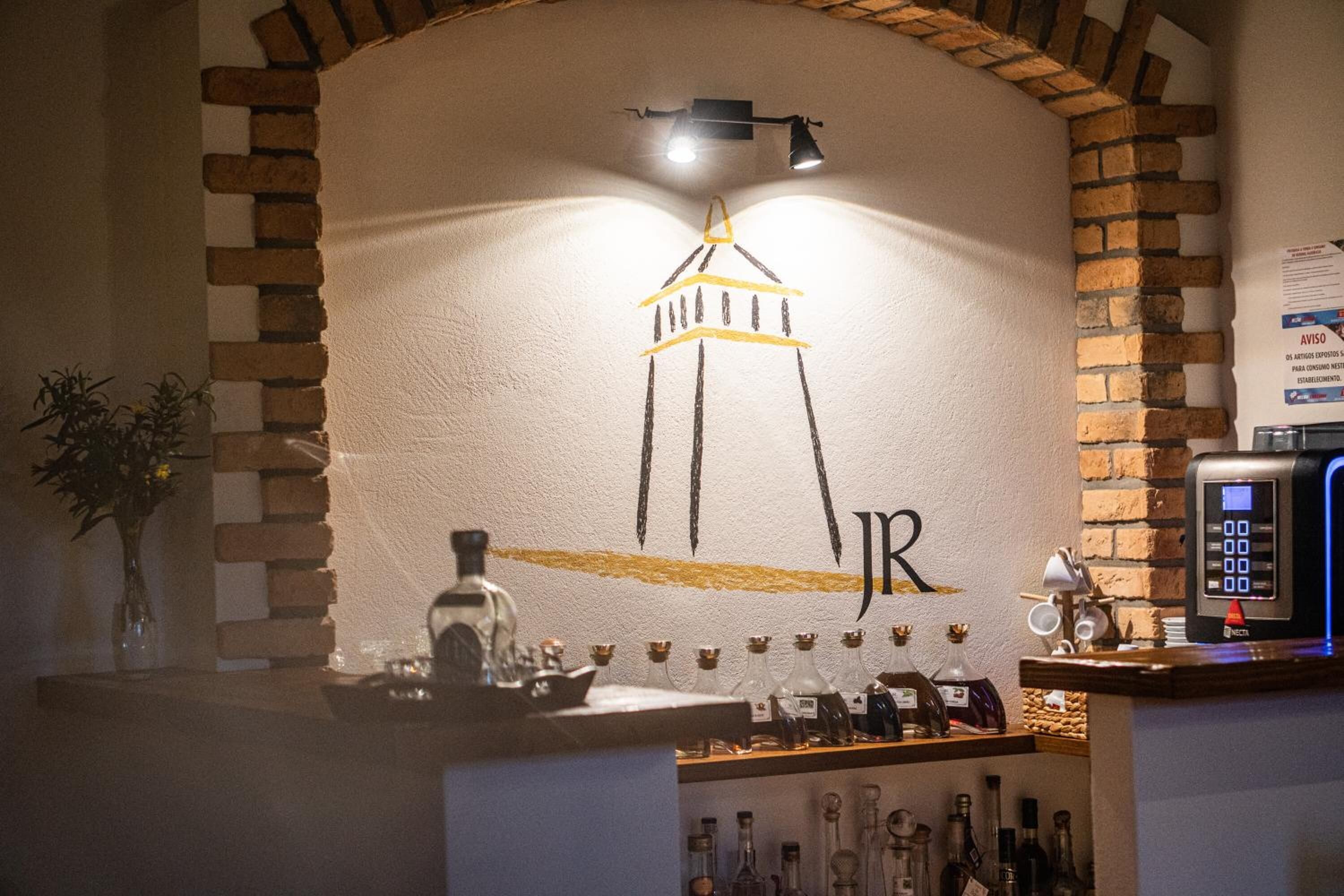 Uma área de bar com arco de tijolos, luminária na parede e um dispositivo digital no balcão.