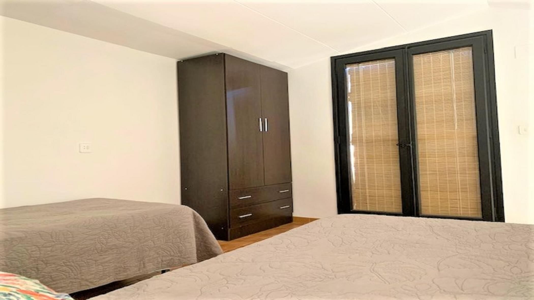 A bedroom with a large wardrobe, a bed, and a window with blinds.