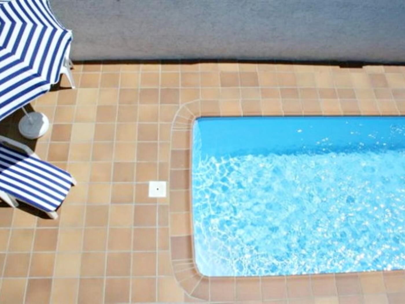A swimming pool with tiled flooring and two striped umbrellas.