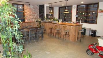 A bar area with stools, a counter, and a motorcycle in a room with brick walls and large windows.