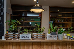 Un mostrador de recepción con plantas en macetas, cajas de madera y carteles que dicen 'KEEP HERE'.