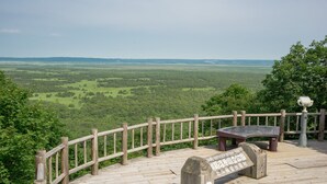 Une plateforme d’observation en bois, dotée d’un banc et d’un panneau d’information, qui offre une vue imprenable sur un vaste paysage verdoyant.