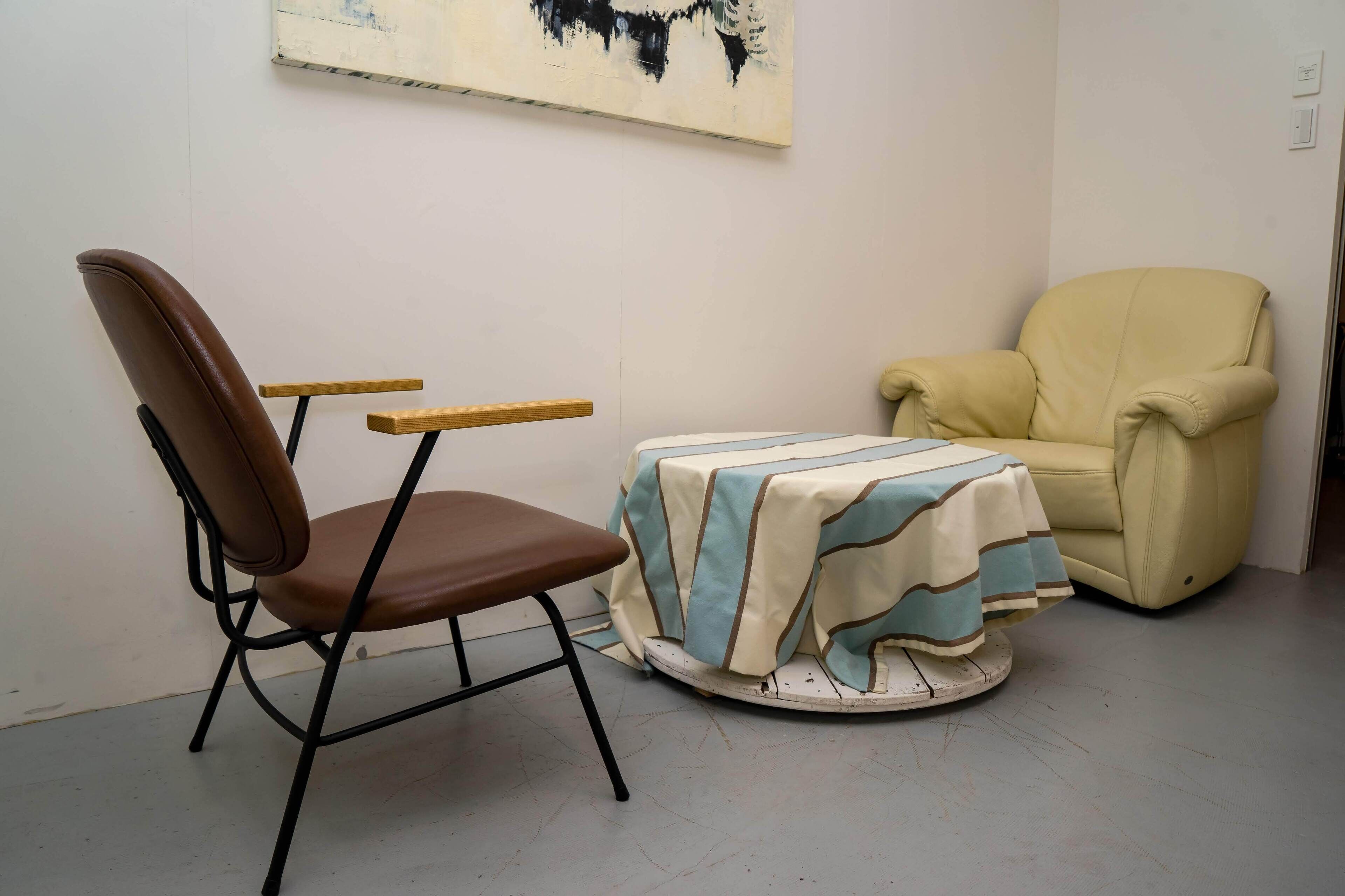 A room with a brown chair, a small table with a striped tablecloth, and a yellow armchair.