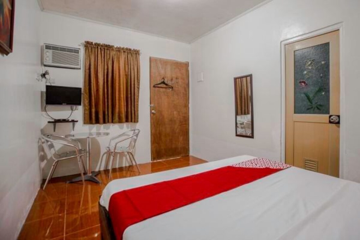A hotel room with a bed, a desk with chairs, a television, and a door.