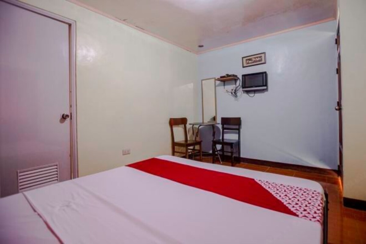 A room with a bed, a desk, a chair, a television, and a door.