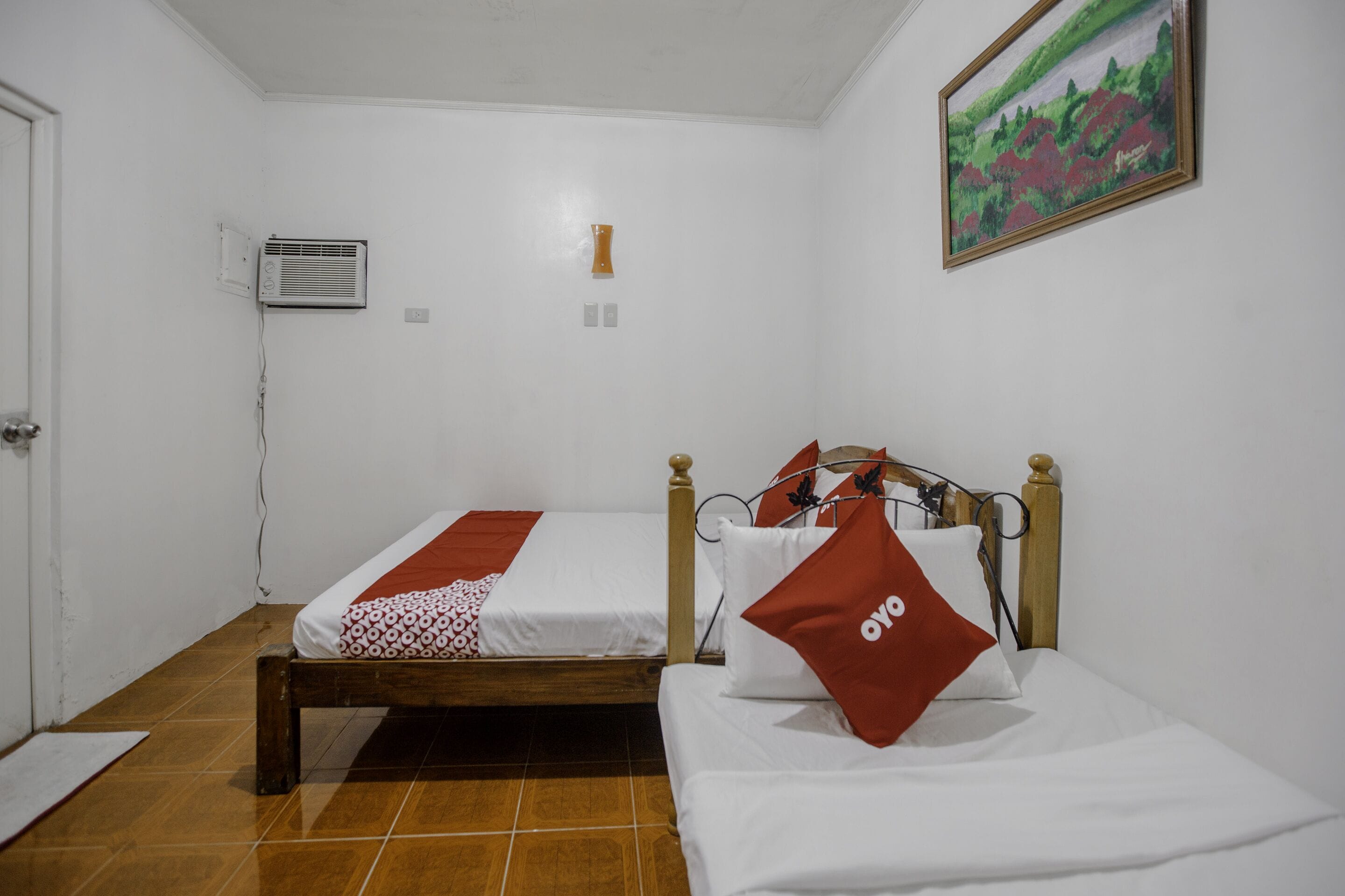 A room with two beds, a painting on the wall, and an air conditioning unit.