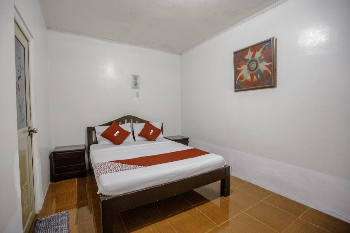 Un dormitorio ordenado con una cama, una mesita de noche, una lámpara de pared y una puerta.