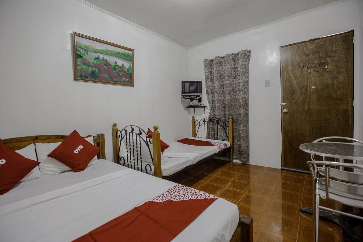 Una habitación con dos camas individuales, una mesita, un televisor y una puerta.