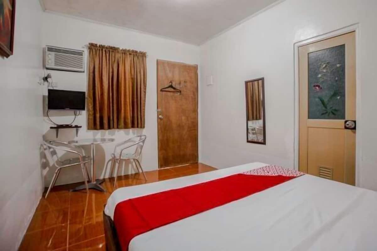 Una habitación de hotel con cama, escritorio con sillas, televisor y puerta.