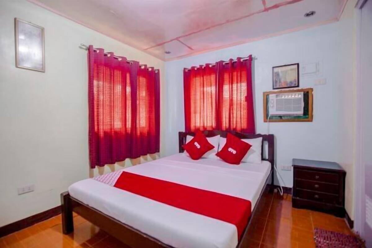 Un dormitorio con cama, dos cortinas rojas, una mesita de noche y un aire acondicionado instalado en la pared.