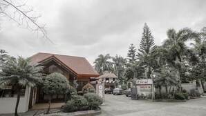 A hotel entrance with a red-tiled roof, a signboard, and a paved driveway.