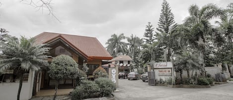 A hotel entrance with a red-tiled roof, a signboard, and a paved driveway.