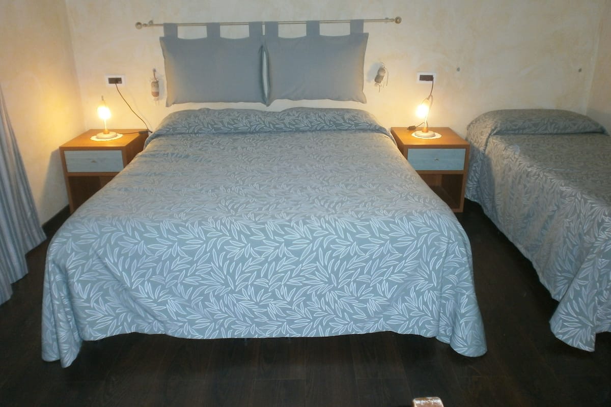 A double bed with a leaf-patterned bedspread, two bedside lamps, and a wooden headboard.
