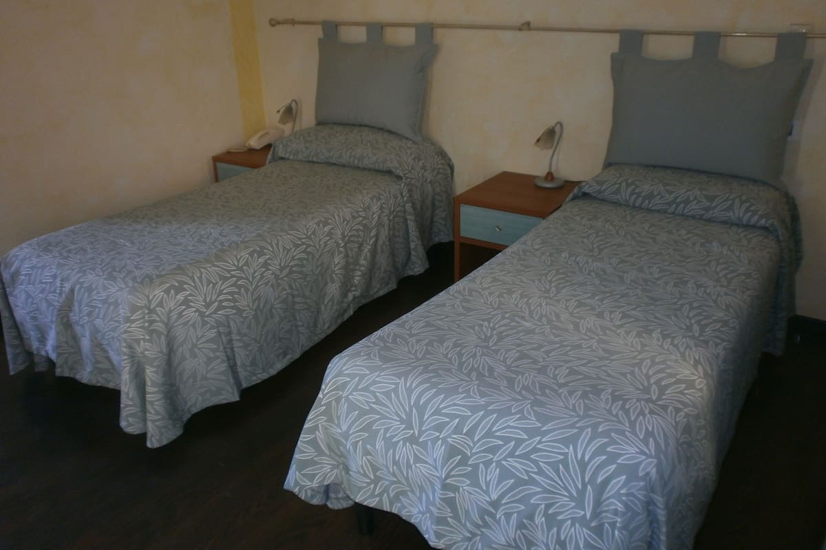 A room with two single beds, each with a nightstand and a lamp.