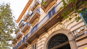 Un edificio con un amplio arco de entrada, varios balcones y carteles de 'Banca Sella' y 'MOMA'.