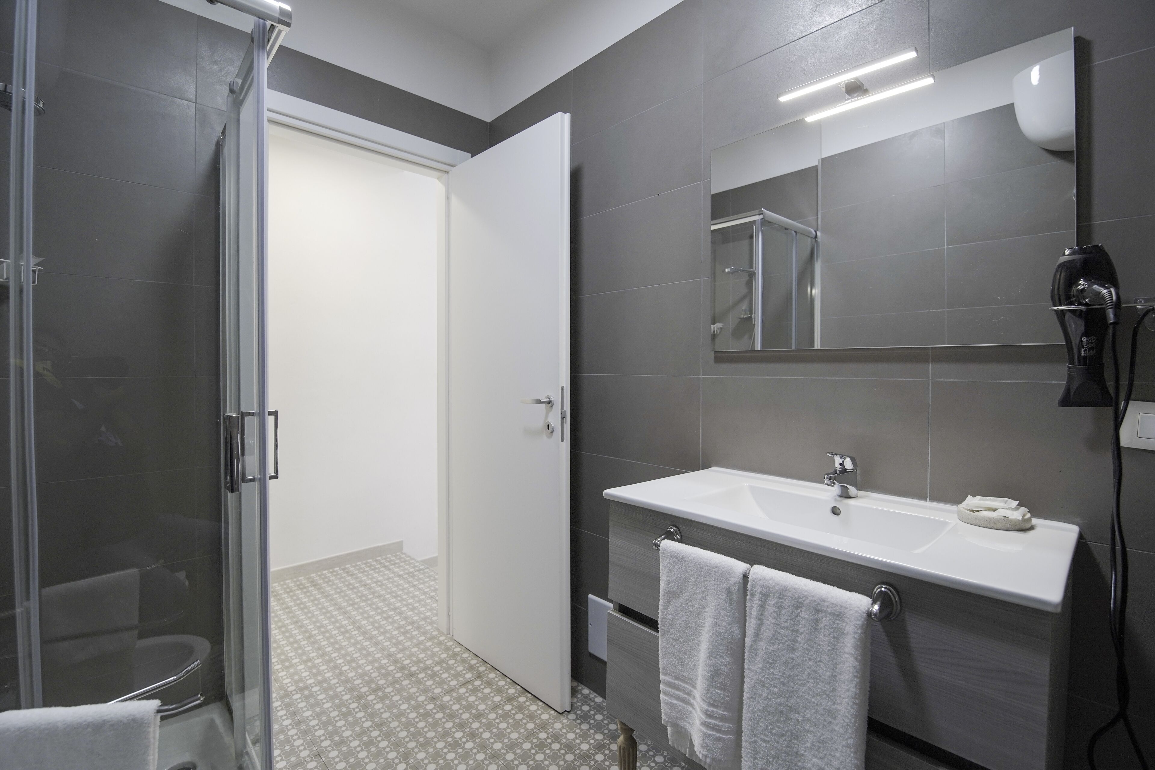 A modern bathroom with a glass shower enclosure, a white sink, and a mirror above it.