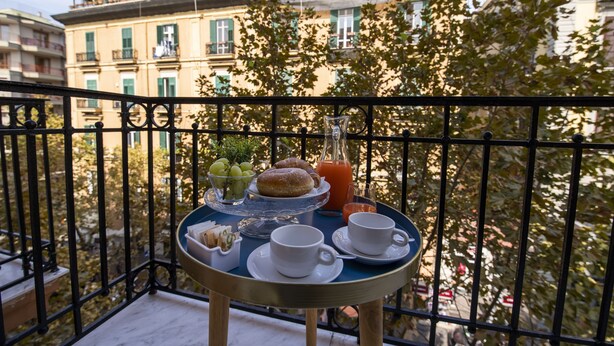 Un balcón con una mesa dispuesta para el desayuno, que incluye bollería, fruta y bebidas.