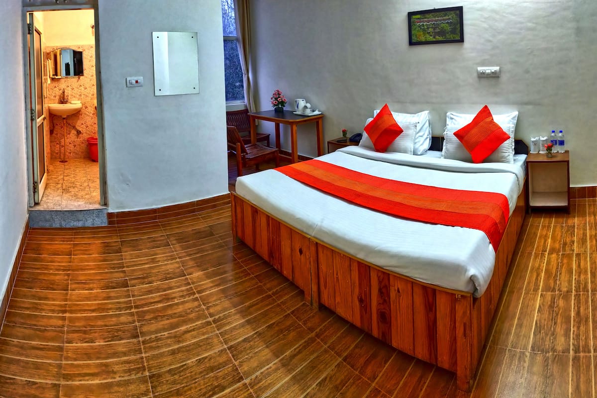 A hotel room with a wooden bed, a small table with a vase of flowers, a nightstand with a lamp, and a view of the outside through a window.