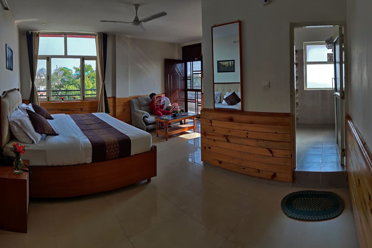 A spacious bedroom with a large bed, a wooden bench, a sofa, and a dining table.