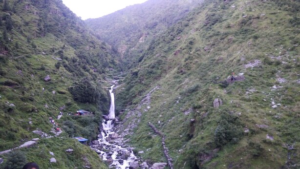 A waterfall in a lush valley with rocky terrain and greenery. - Highland Village Resort (Dharamshala)