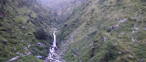 A waterfall in a lush valley with rocky terrain and greenery.