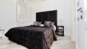 A bedroom with a large bed, a dark headboard, and a nightstand with a lamp. - Reale Luxury home  (Roma)