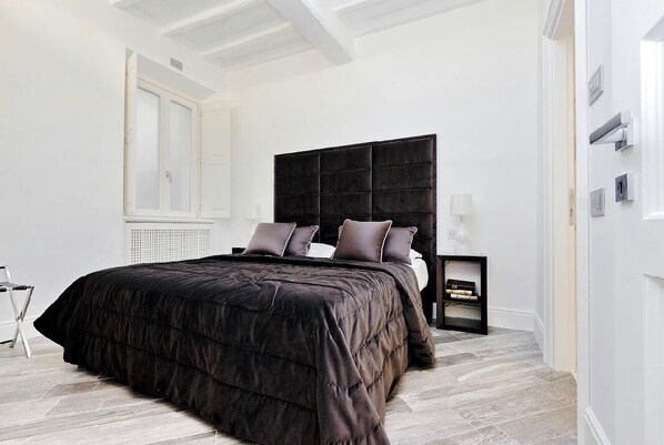 A bedroom with a large bed, a dark headboard, and a nightstand with a lamp. - Reale Luxury home (Roma)
