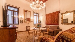A room with a wooden desk, a round dining table with chairs, a sofa, a chandelier, and large mirrors. - Fenice Backstage over Canal (Venice)