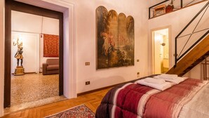 A bedroom with a bed, a large painting, a staircase, and a hallway leading to another room. - Fenice Backstage over Canal (Venice)