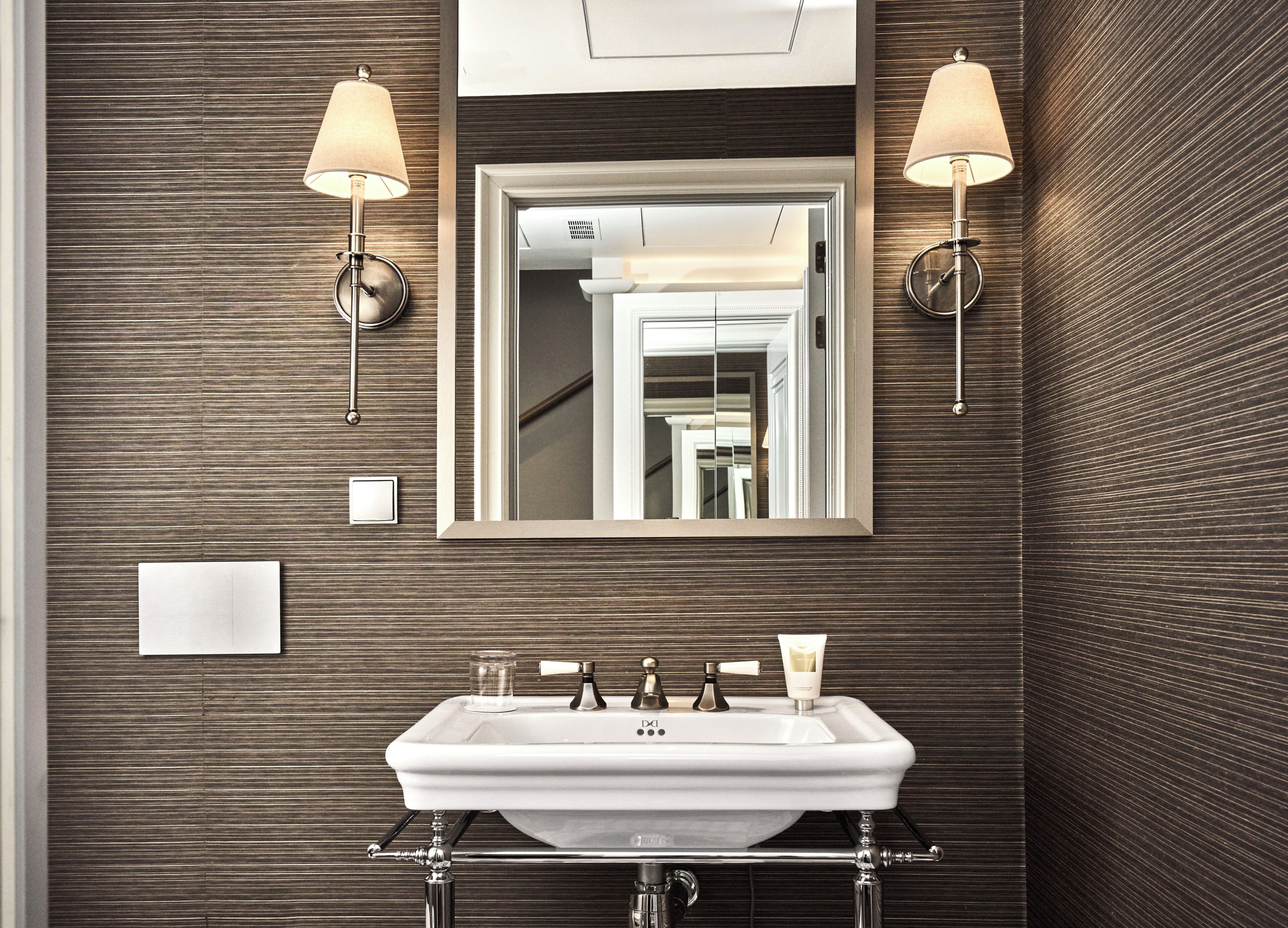 Un baño moderno con un espejo grande, dos lámparas de pared, un lavamanos blanco y un perchero para toallas.