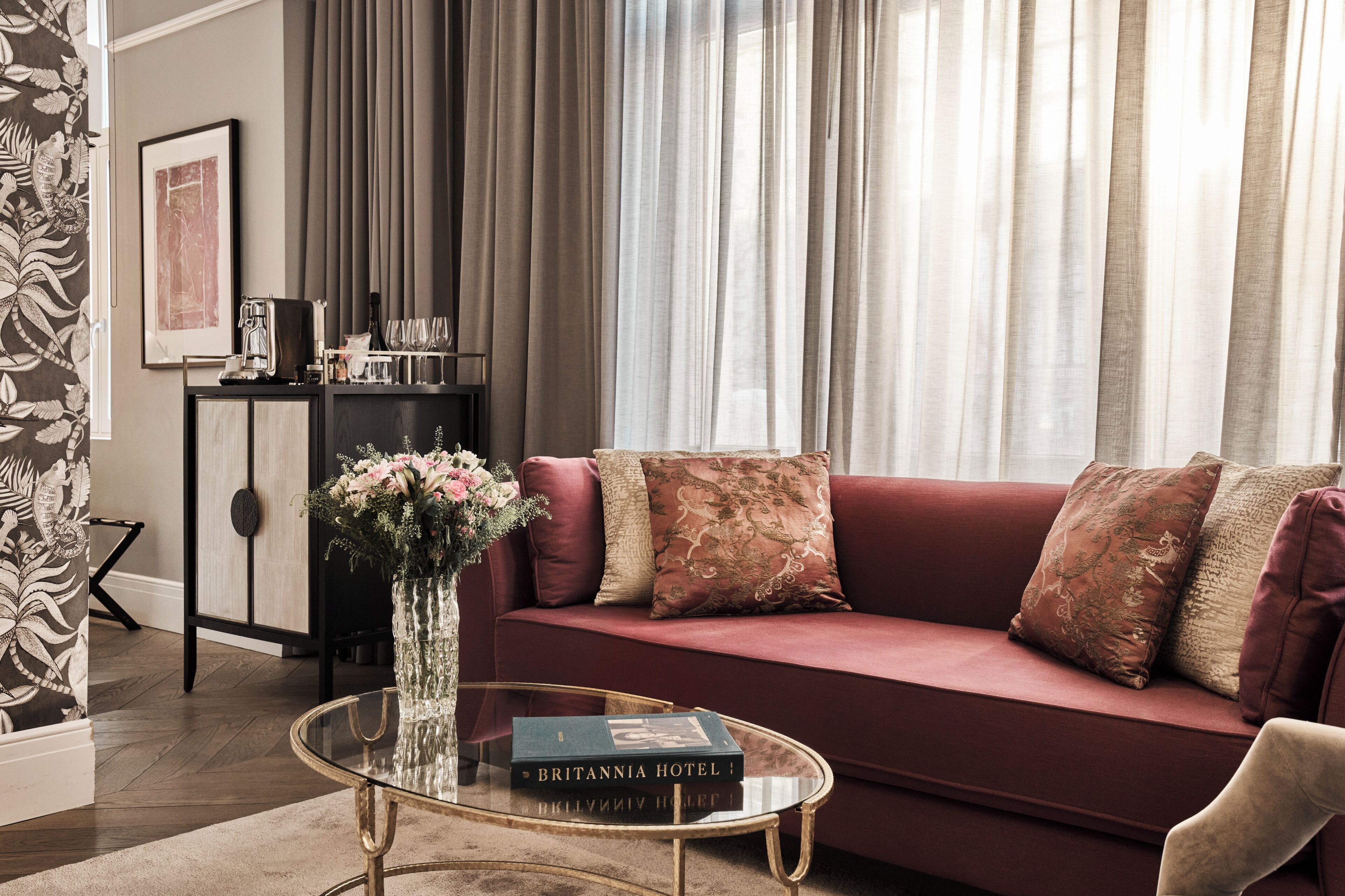 A living room with a red sofa, a glass coffee table, and a vase with flowers.