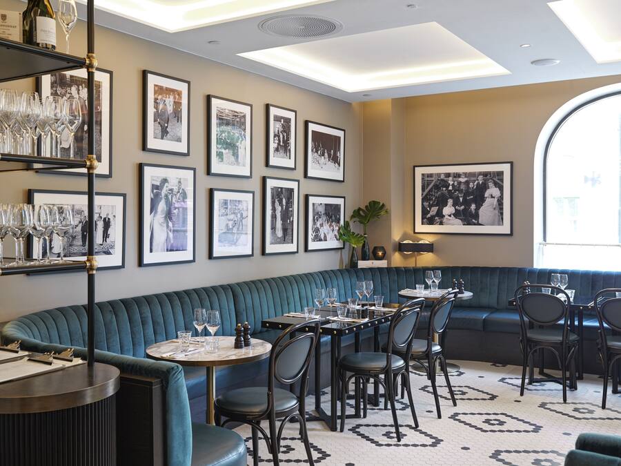 Un restaurante con una zona de estar con bancos acolchados azules, fotografías en blanco y negro en la pared y una mesa redonda con sillas.