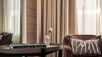 A leather sofa with a patterned pillow, a small table with a book titled 'BRITANNIA HOTEL,' and a vase with a single white flower.