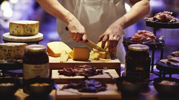 Eine Person schneidet Käse auf einem Holzbrett, umgeben von verschiedenen Käsesorten und Fleisch.