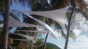 A beachside dining setup with tables covered in white tablecloths, surrounded by palm trees and a view of the sea.