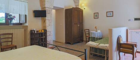 Una habitación con una cama, un armario de madera, una mesa con una silla, una mesita de noche con una lámpara y una ventana con cortina.