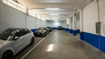 Un parking à plusieurs niveaux avec des murs blancs et bleus, plusieurs voitures garées et un éclairage fluorescent au plafond.