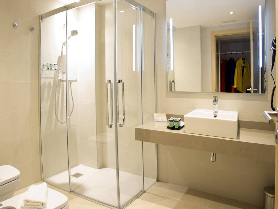 Un baño moderno con ducha de vidrio, un lavamanos blanco y un espejo grande.