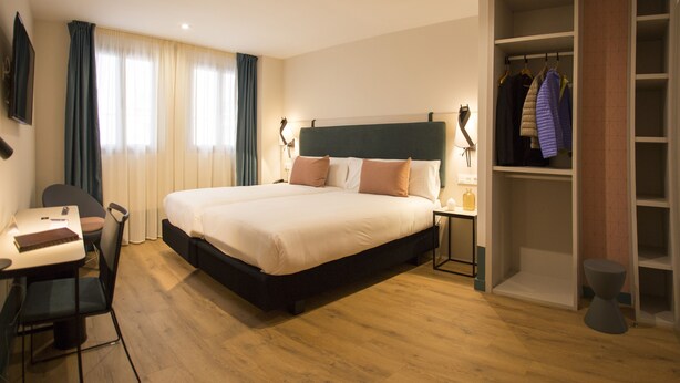 Ein Hotelzimmer mit einem großen Bett, einem Schreibtisch mit Stuhl, einem Kleiderschrank und einem Nachttisch mit Lampe.