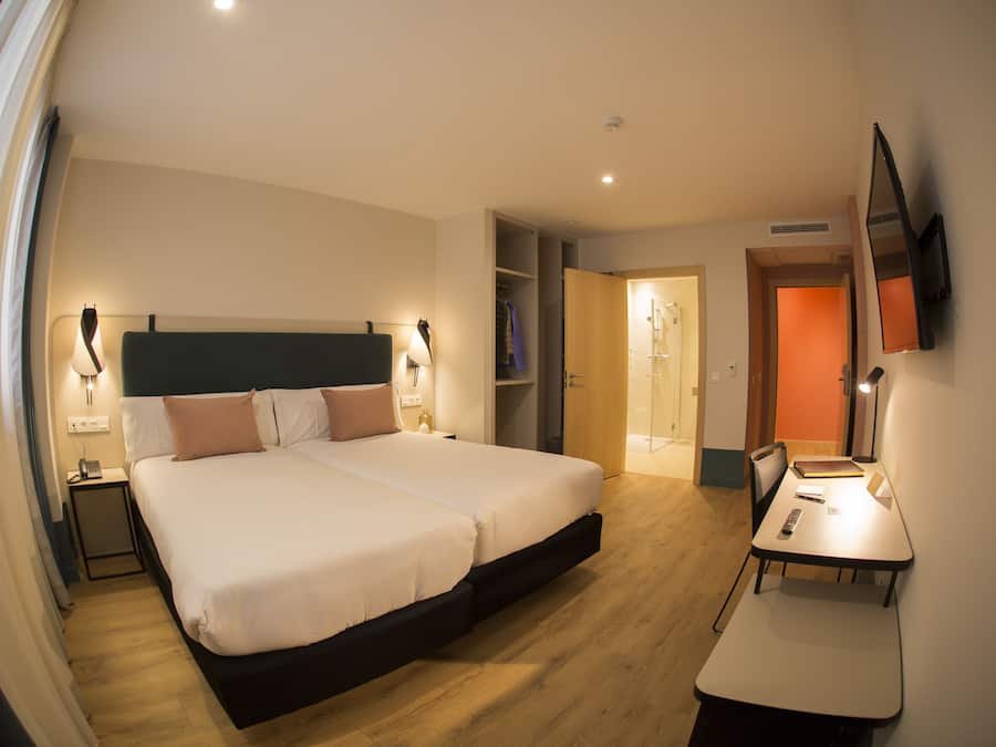 Une chambre d’hôtel moderne dotée d’un grand lit, de tables de chevet, d’un bureau et d’un téléviseur fixé au mur.
