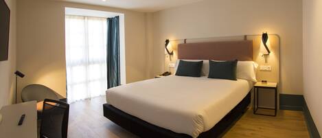 Una habitación de hotel con una cama grande, mesitas de noche, un escritorio y una silla.