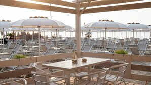 A beachside seating area with umbrellas and lounge chairs, a table with chairs, and a view of the beach. - Hotel Continental (Pietra Ligure)