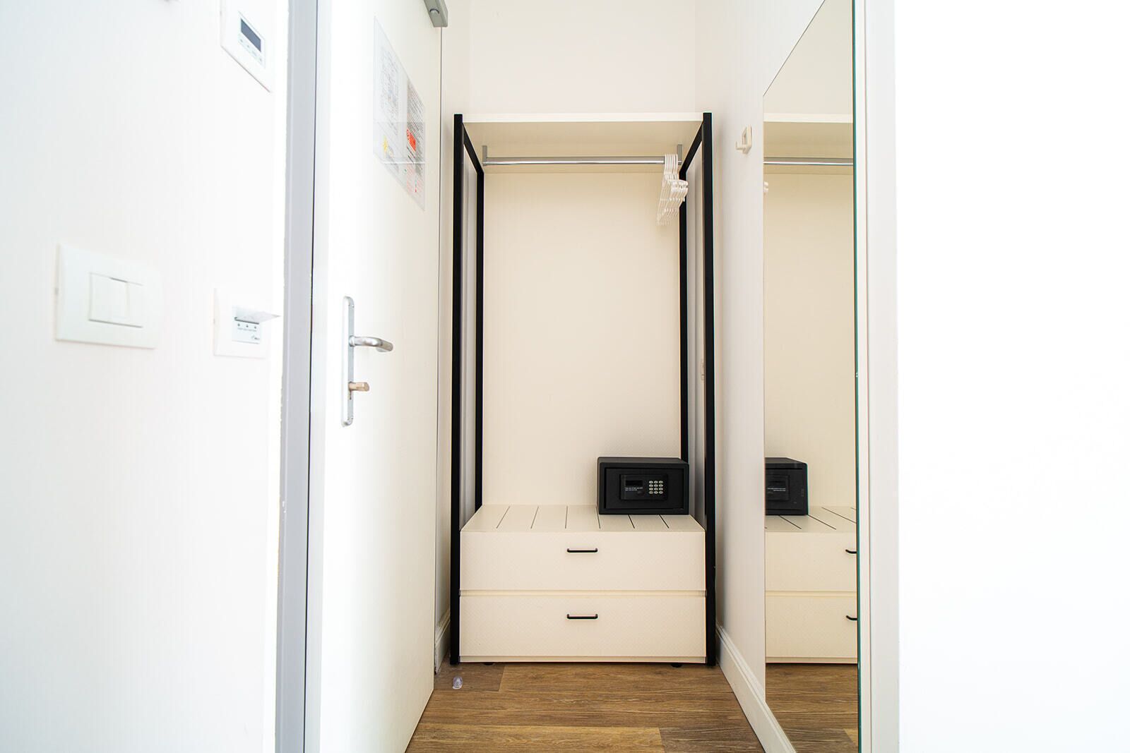 Un corridoio stretto che conduce a una camera da letto con un letto, un comodino e uno specchio.