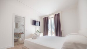 A hotel room with a bed, a TV, a bathroom with a mirror, and a window with curtains. - Hotel Continental (Pietra Ligure)