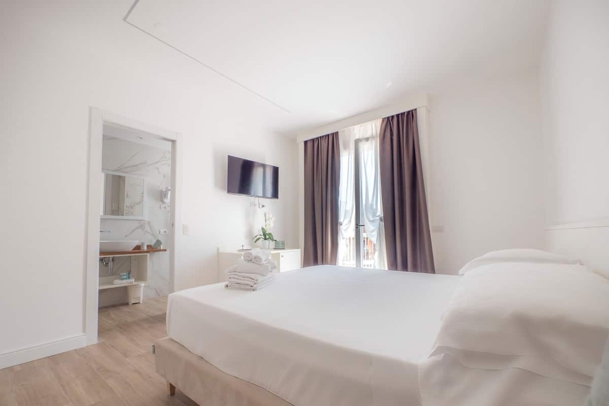 A hotel room with a bed, a TV, a bathroom with a mirror, and a window with curtains.