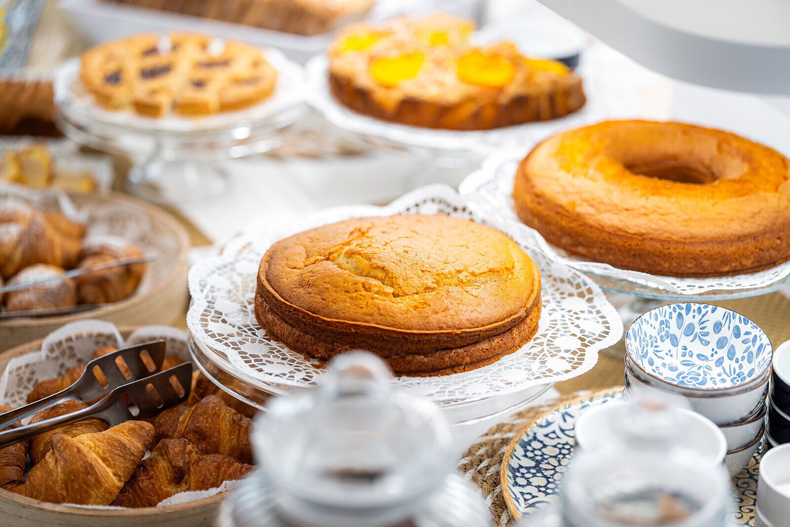 A variety of baked goods on display, including cakes and pastries, arranged on a table with a lace doily.