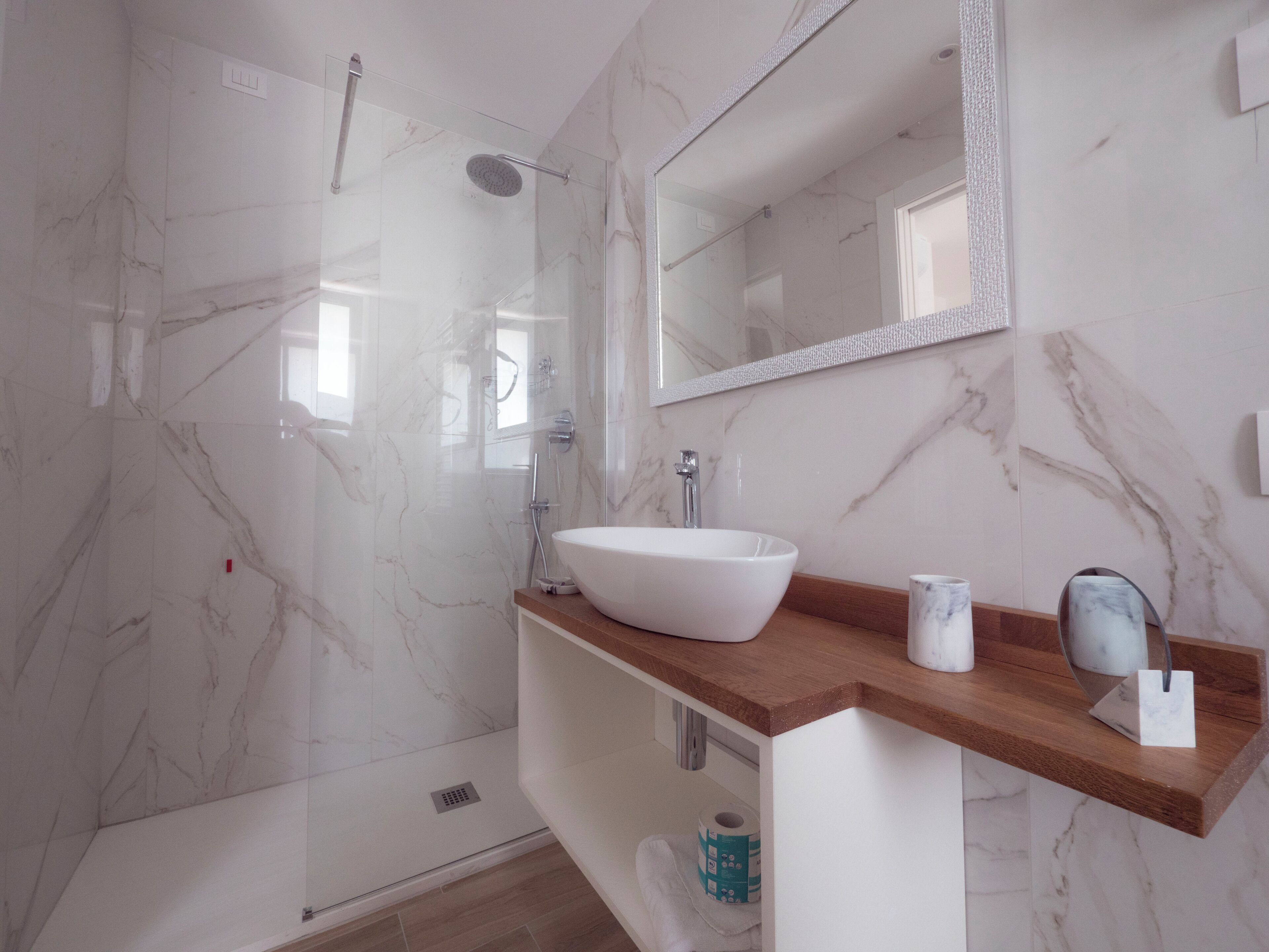 A modern bathroom with a glass-enclosed shower, a white vessel sink, and a marble-tiled shower wall.