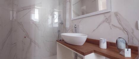 A modern bathroom with a glass-enclosed shower, a white vessel sink, and a marble-tiled shower wall.