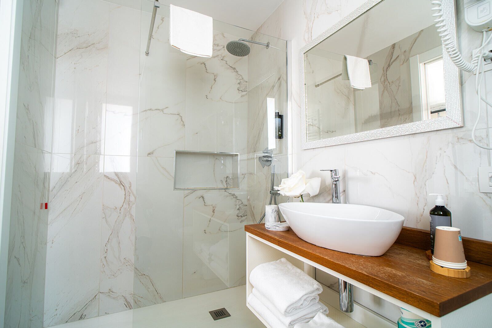 Een badkamer met een marmeren wand, een witte wasbak, een spiegel en een douche.