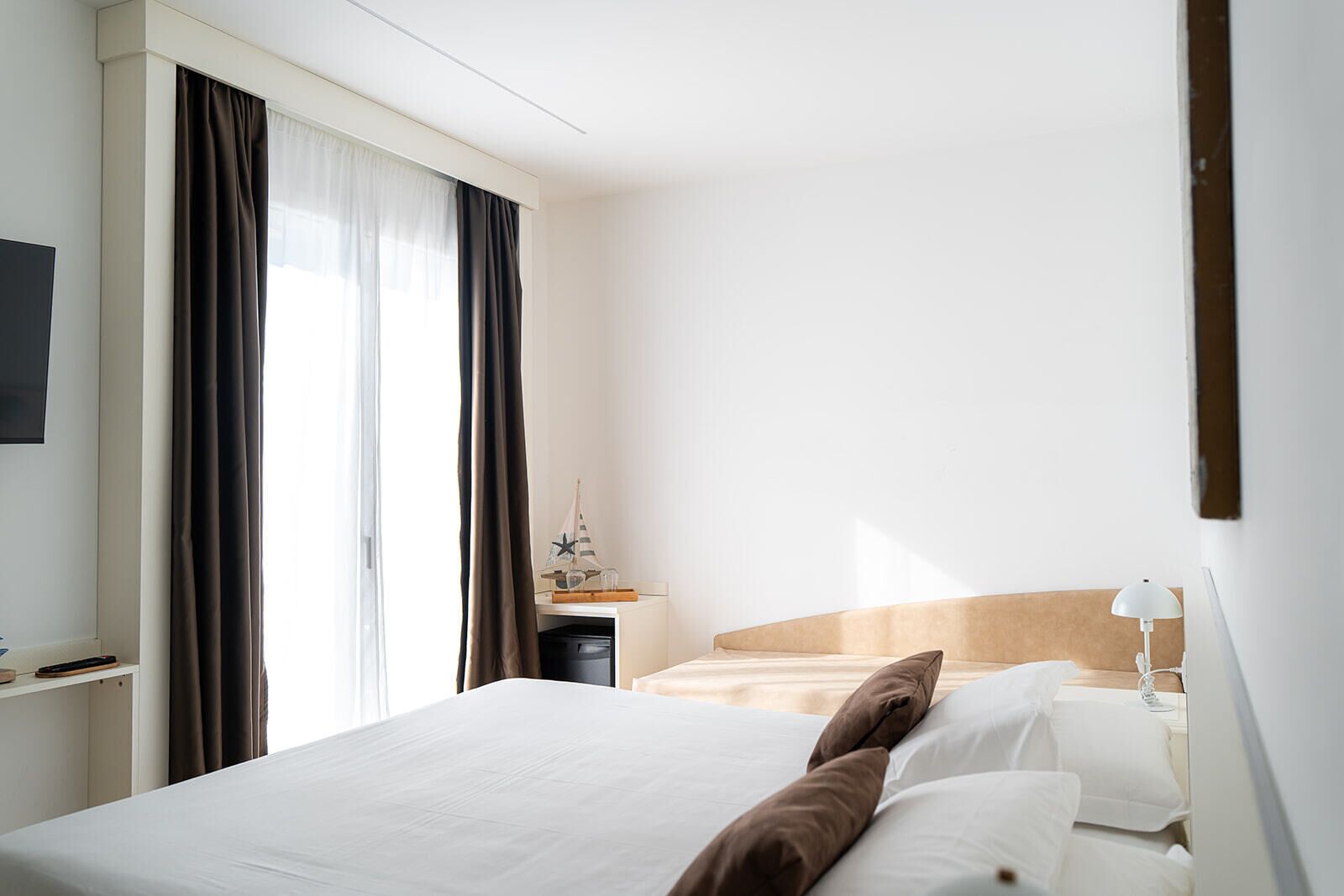 A hotel room with a bed, a nightstand, a lamp, and a window with curtains.
